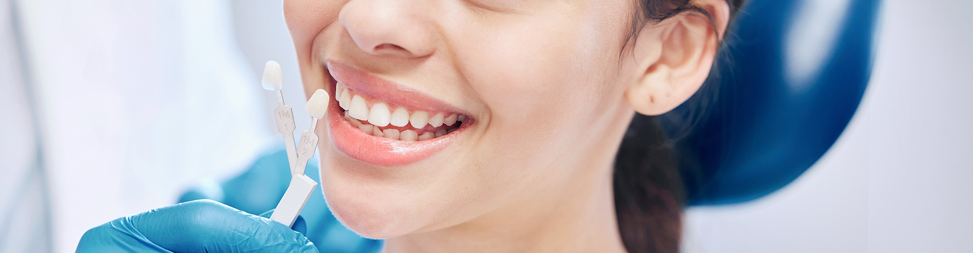 gloved hands-holding tooth shade-matching tool against woman's smile